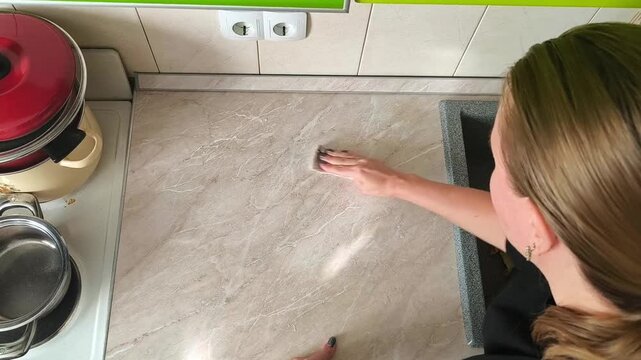 A woman cleans the kitchen countertop next to the sink, a household scene of cleaning, caring for the work area and maintaining cleanliness.
