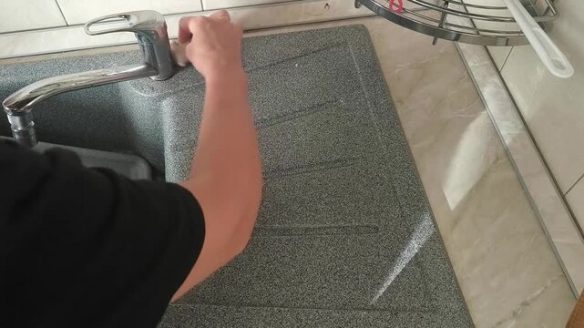 A woman wipes the kitchen surface next to the sink, a household scene of home care, cleanliness and daily cleaning.
