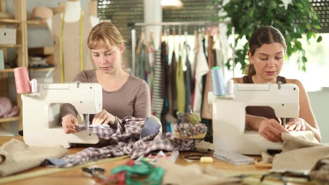 Two attentive young female dressmakers working with sewing machine in tailor's workshop. High quality 4k footage