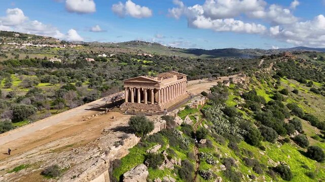 Frontal drone view of the Temple of Concordia surrounded by hills and greenery in Agrigento, Sicily.
