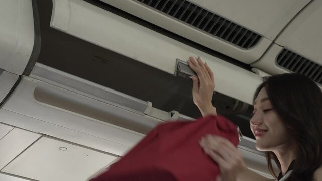Smiling female passenger reaching up to open overhead bin inside an airplane cabin, travel concept.