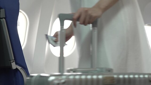 Passenger cabin interior of an airplane with window seats, blue seat, and traveler holding a rolling suitcase handle, suggesting business travel and air transport.