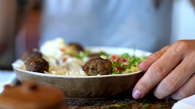 Macro shot of young woman hand with fork eating tasty healthy food from ceramic plate on table next to opened book bokeh blurred face background of girl enjoying meal in modern restaurant cafe 4k