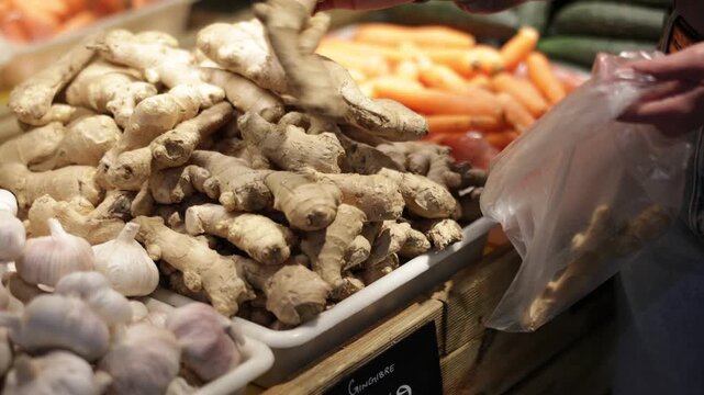 Woman hands hold a close up of ginger root and put it in a bag for packaging. Customer prepares to weigh ginger in a supermarket. High quality 4k footage