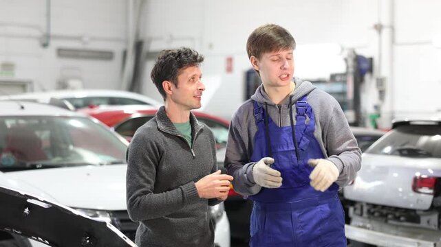 Adult car owner discusses with a young auto mechanic the cost and time of car repairs at a car service center. High quality 4k footage