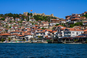 The historic town of Ohrid cascades down a hill to Lake Ohrid, crowned by Samuil's Fortress from which the Macedonian flag proudly flies. Traditional architecture and vibrant red roofs stand out © Danica Chang