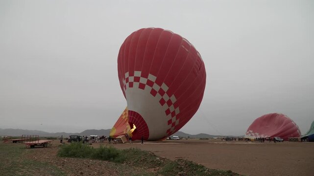 Deflating hot air balloon on overcast day in open field, calm atmosphere
