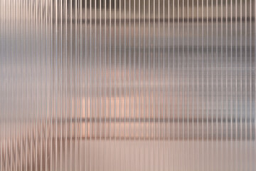 A full frame view shows the surface of a semi transparent ribbed glass panel with vertical textured lines and a soft brown background showing through. © nahhan