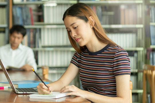 Female asian student studying and reading book in library
