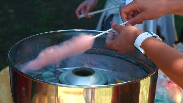 Preparing Pink Cotton Candy At Festive Outdoor Fair showing the process of wrapping sweet sugar strands onto a stick during an outdoor event and leisure activity