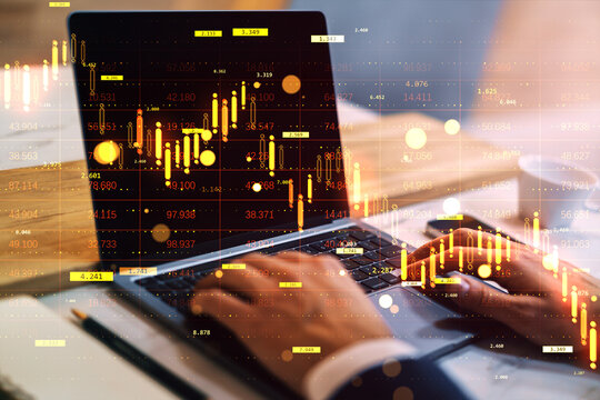 Business trader working on laptop with glowing financial charts and digital market indicators overlaid on office desk background in abstract style.