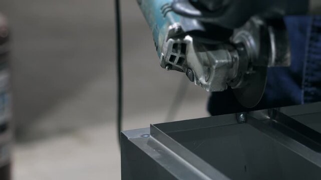 Close up of worker cutting metal with angle grinder in factory workshop, sparks flying during metalworking and industrial process.