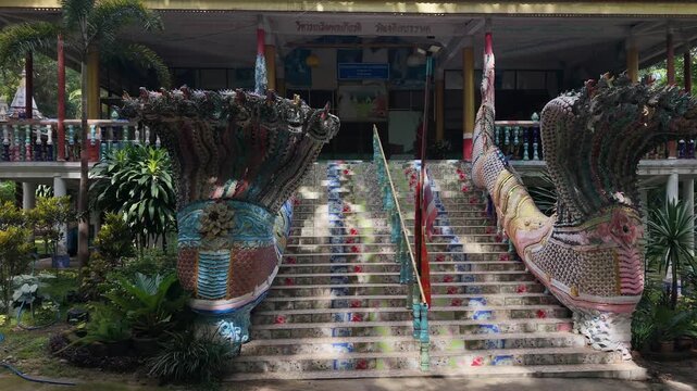 A wide, steady shot of an ornate, colorful Naga dragon staircase sculpture leading up to a temple in a garden setting.