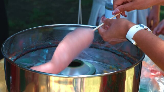 Preparing Fluffy Pink Cotton Candy At Outdoor Fair showing the process of shaping a sweet dessert from sugar strands during a festive outdoor event