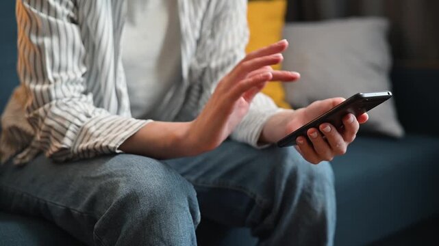 A person is sitting on a couch and using a smartphone. They frequently tap and swipe the screen, mobile phone is annoying, it doesn't work well and the person hits the phone screen.