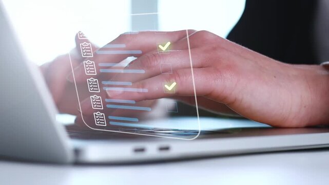 Hands typing on a laptop with task lists and checkmarks visible on the screen in a working environment during daytime.