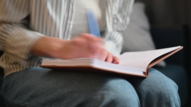 A person is sitting comfortably while writing in a notebook using a blue pen. Close-up of a hand aggressively crossing out items in a diary