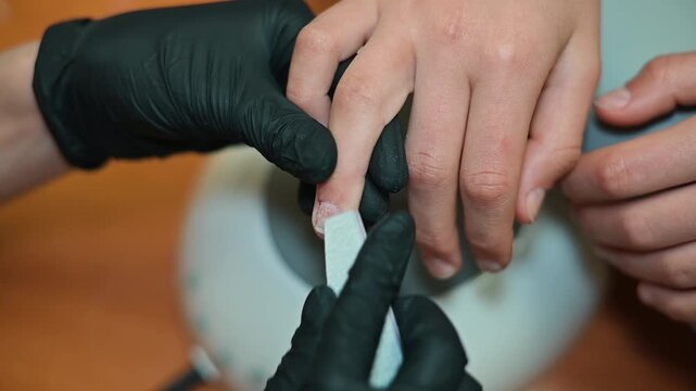 A nail technician carefully attends to a client's nails using a file to shape and smooth them