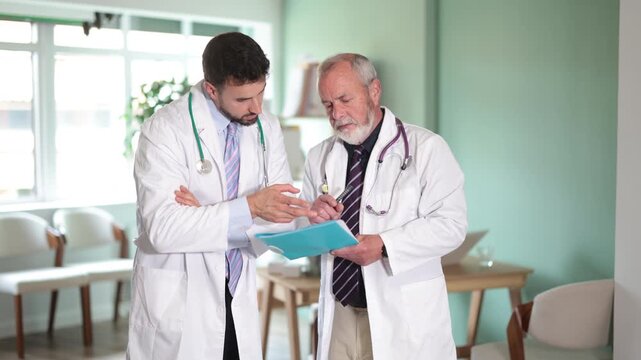 Two doctors review or read medical documents. Colleagues consult, discuss complex and confusing clinical case, consider treatment options, and discuss hypotheses. 
