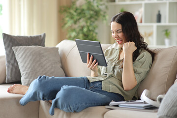 Fototapeta premium Excited student celebrating good news holding tablet