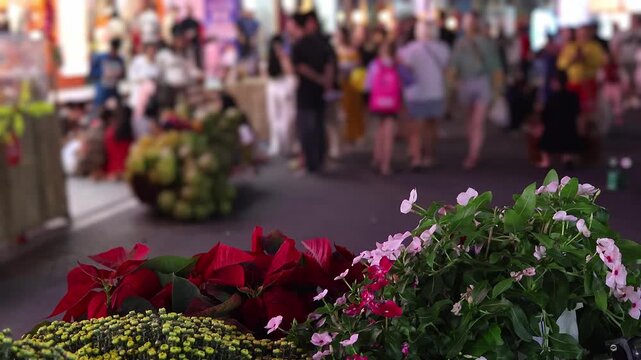 Night street market with colorful lanterns, flower decorations and crowd walking during Tet celebration in Vietnam. Concept of vibrant nightlife, asian culture, festival atmosphere.