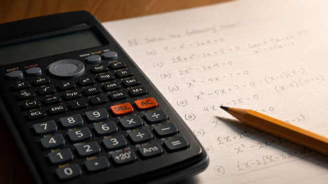 Back to school. Close-up of a scientific calculator placed on a math homework sheet with handwritten equations, a pencil resting nearby.