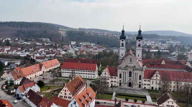 Drone view of Zwiefalter Munster with village streets, red roofs, forested hills, and valley landscape in Baden Wurttemberg, Germany.