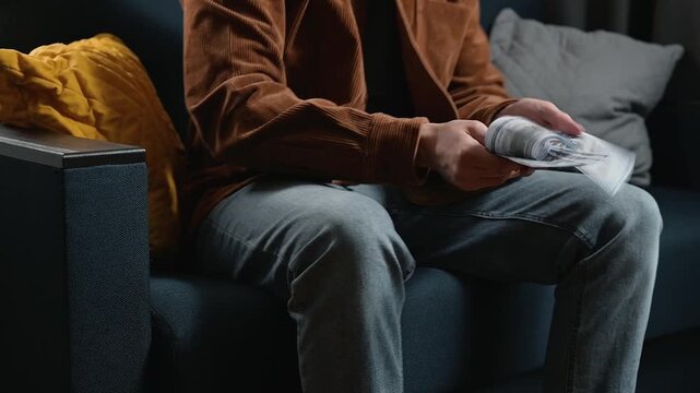 A close-up of an unrecognizable male character joyfully holding a pile of money in his hands, dancing while sitting on a sofa and shaking dollars
