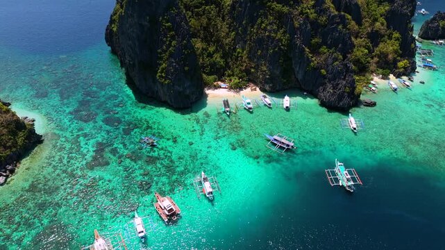 Aerial drone view of Shimizu Island near El Nido, Palawan, Philippines with turquoise water, tropical limestone cliffs, white sand beach, and traditional boats.