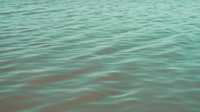 Teal green water surface texture with gentle ripples and soft reflections, full frame view.