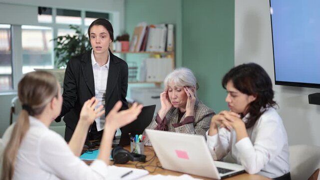 Young woman stands at office desk and scolds group of upset women in office