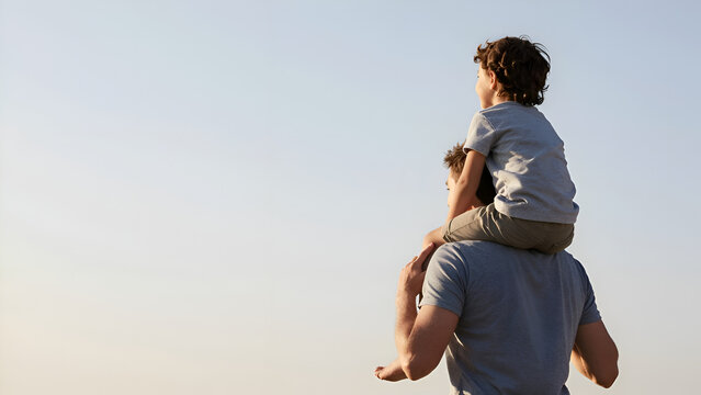 Happy father carrying his little son on shoulders against clear blue sky