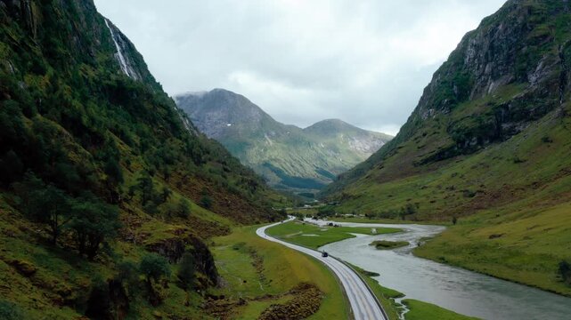 High-angle drone footage of majestic mountain peaks and a winding river road in Klakegg, Norway. Cinematic summer landscape featuring vehicles driving through a lush green glacial valley