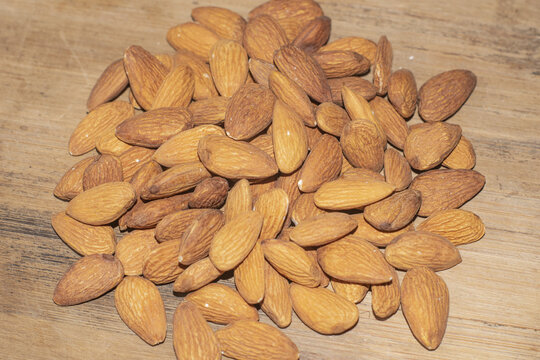 Pile of raw almonds scattered on a rustic wooden surface 