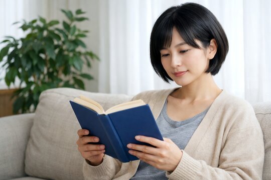リビングのソファーに座りリラックスしながら青い表紙の本を読んでいる一人の若い女性