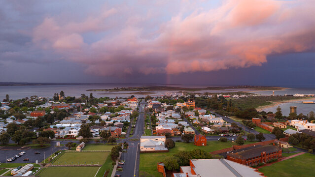 Aerial view of a rainbow in a dramatic coloured sky over historic buildings in a coastal town
