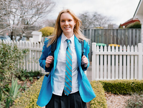 Teenage girl in school uniform stands along a curved brick path of their new home