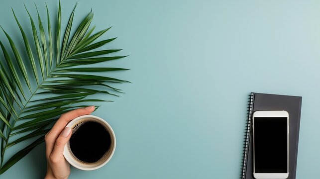 Overhead view captures a hand holding dark beverage next to foliage and modern electronic device