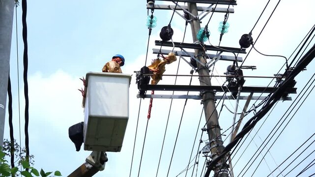 Two Utility Lineworkers Wearing High-Visibility PPE Performing Maintenance on High-Voltage Overhead Distribution Lines