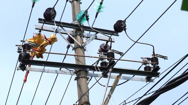 Manual recloser and isolator repair. Yellow cloth hangs next to green cloth. Power lines stretch across the sky. This scene suggests a rural or suburban setting.