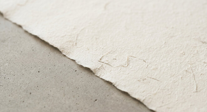 Close-up of textured handmade paper with a deckle edge on a smooth grey concrete surface