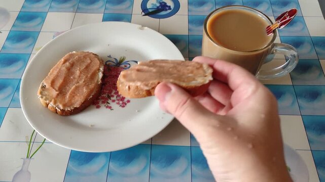 Person biting into caviar sandwich then putting it back on plate with coffee mug on table, first person view