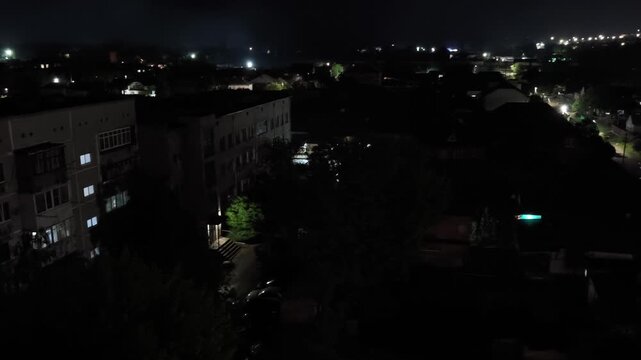 Night cityscape from above with lights roofs and trees, camera zooming in at end