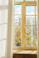 Fototapeta premium Warm light streams through rustic wooden window revealing autumn trees and blue sky.