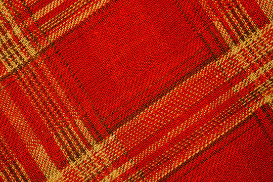 Red and tan plaid woven textile texture for background Close up of red woven fabric with diagonal plaid texture, textile surface details