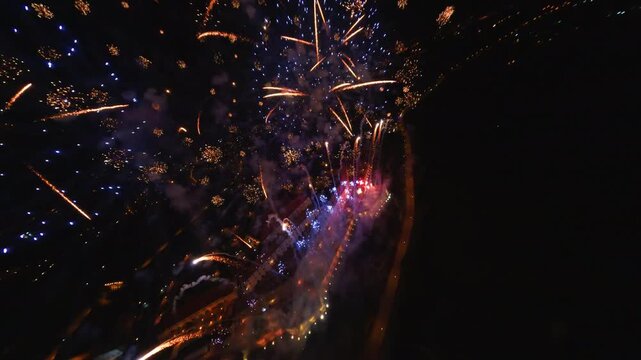 FPV aerial view of colorful fireworks exploding with bright sparks and light trails against the dark night sky over Novi Sad, Vojvodina, Serbia.