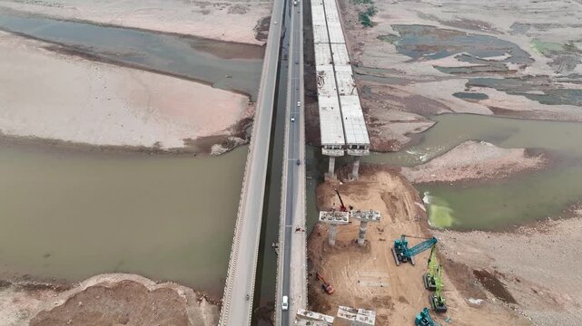 Top-down aerial of new bridge construction over Tawi river in Jammu. High-angle aerial drone footage capturing the construction of a massive new highway bridge.