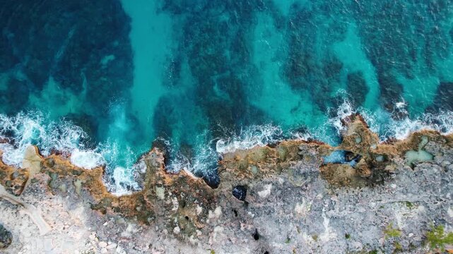 top down shot of cliffs with blue crystal water crashing on cliff side
