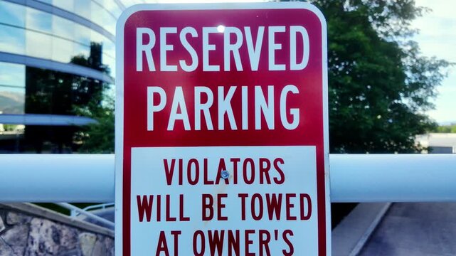 Reserved Parking Violators Will Be Towed At Owner&rsquo;s Expense Red and White Sign with Business Complex Buildings in Background straight on front shot in parking lot trees in background