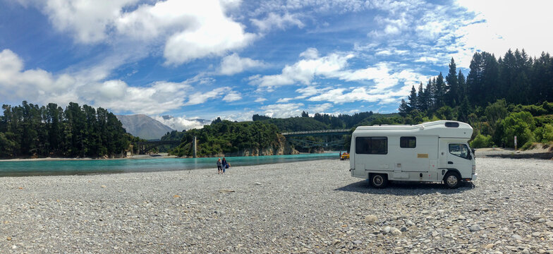 Camper on riverbed next to the Rakaia River with Rakaia Gorge Bridge in background.
